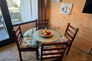 Een ronde glazen tafel met een fruitschaal, omringd door houten stoelen met kussentjes.