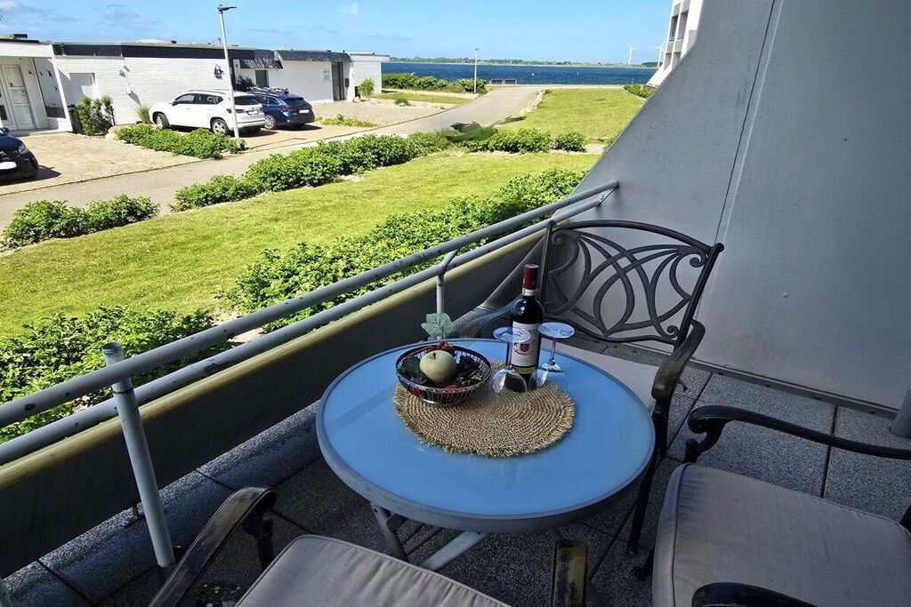 Een balkon met een tafel gedekt voor twee personen, een fles wijn en een schaal met fruit.