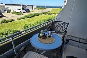 Un balcon avec une table dressée pour deux personnes, une bouteille de vin et un panier de fruits.