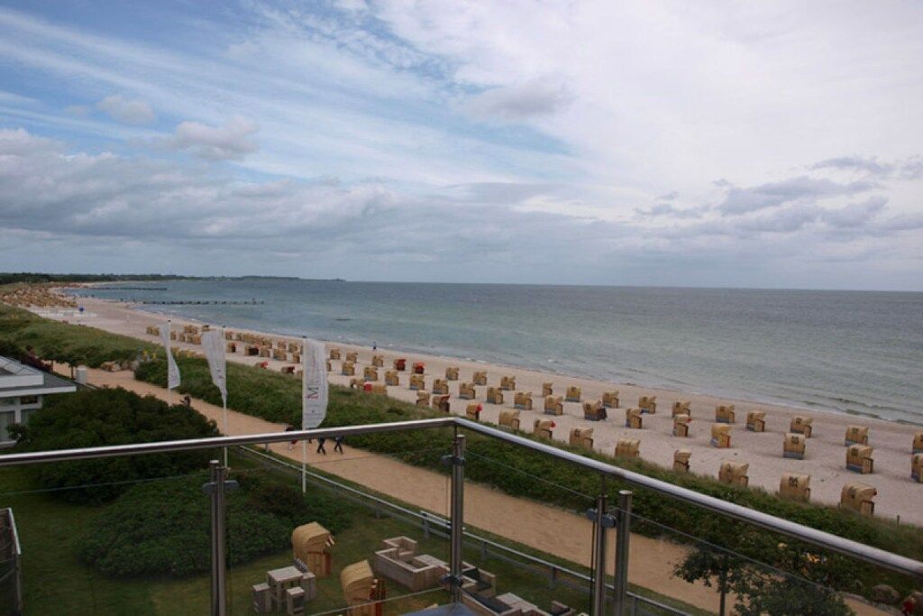Une vue sur la plage depuis un balcon, avec des chaises longues et des drapeaux.
