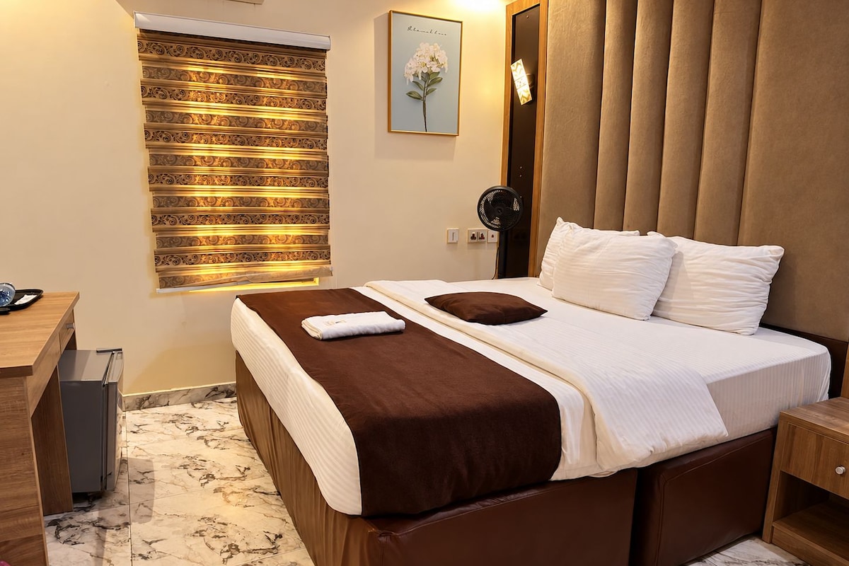 Une chambre d’hôtel avec un lit, une table de chevet et un ventilateur fixé au mur.
