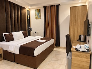Une chambre d’hôtel avec un grand lit, un bureau avec une bouilloire et un tableau au mur.
