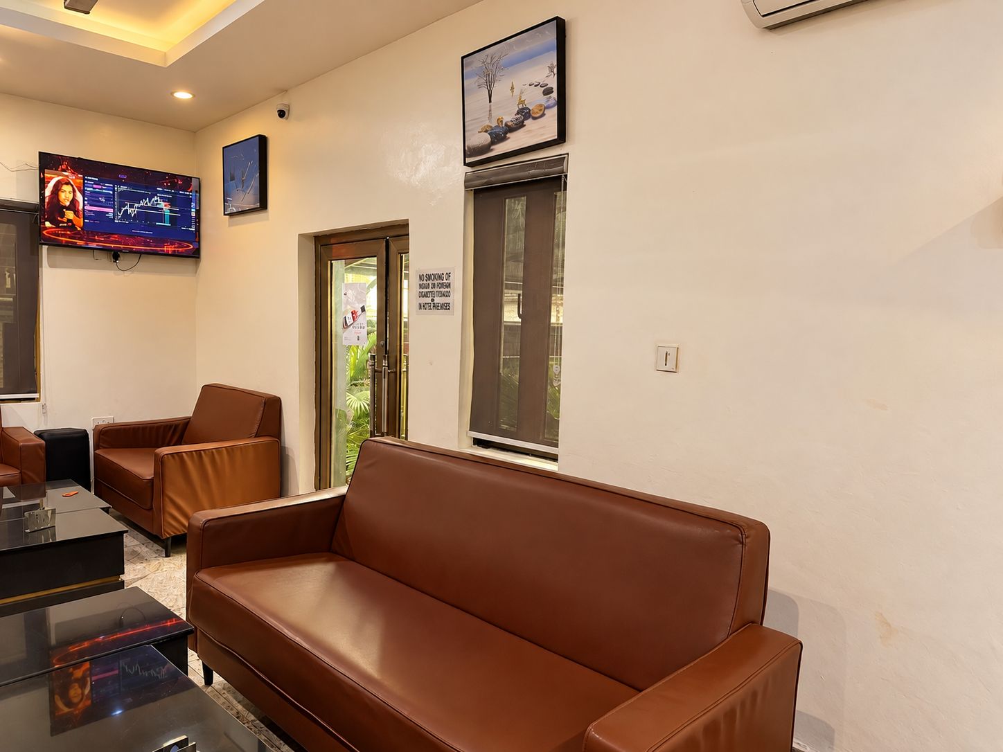 A waiting area with leather sofas, a flat-screen TV displaying financial charts, and a window with a view of the outdoors.