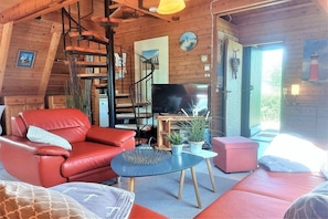 A cozy cabin interior with a red leather sofa, a television, and a staircase leading to a loft area. - Holiday home in Damp with swimming pool (Damp)