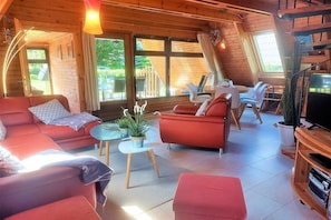 A cozy cabin interior with a sofa, armchairs, a small table with plants, a TV stand, and a dining area with chairs. - Holiday home in Damp with swimming pool (Damp)