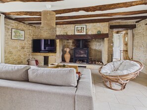 A stone-walled living room with a fireplace, a television, and a wicker chair. - House for 8 with heated pool (La Bachellerie)