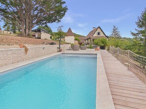 En swimmingpool med træterrasse og stenvæg, omgivet af huse og træer.