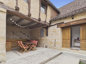 A stone building with a tiled roof, a wooden table with chairs, and a small kitchen area. - House for 8 with heated pool (La Bachellerie)