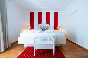 A bedroom with a white bed, red accent walls, and a white chair. - Apartment with 1 bedroom (Heiligenblut am Großglockner)
