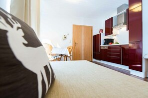 A compact room with a bed, a small dining table, and a kitchenette with dark cabinets and a microwave. - Apartment with 1 bedroom (Heiligenblut am Großglockner)