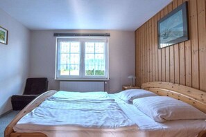 Une chambre à coucher avec un lit double, une chaise, une fenêtre avec des stores et un mur en bois.