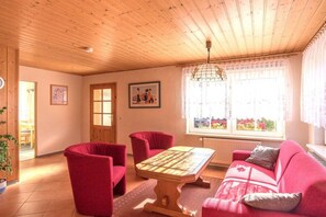 Une pièce avec un plafond en bois, un canapé rouge, un fauteuil rouge, une table basse en bois et une fenêtre donnant sur un beau paysage.
