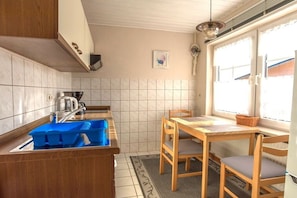 A kitchen with a sink, a blue dish rack, a window with a view, and a table with chairs. - Holiday apartment with 1 bedroom (Middelhagen)