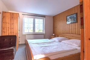 A bedroom with two beds, a chair, a window, and wooden paneling on the walls. - Holiday apartment with 1 bedroom (Middelhagen)