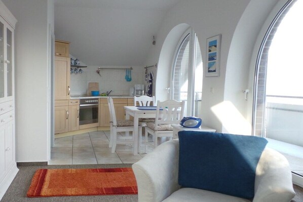 A compact living space with a kitchenette, dining area, and a sofa with a blue cushion. - Holiday apartment with 2 bedrooms (Schönberger Strand)
