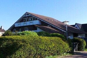 A two-story residential building with a sloped roof, a balcony on the upper floor, and a well-maintained hedge in the foreground. - Holiday apartment with 2 bedrooms (Schönberger Strand)
