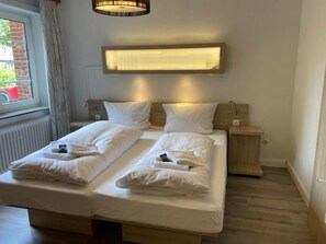 A double bed with two pillows, a bedside table, a wall-mounted light, and a window with curtains. - Holiday Apartment With 1 Bedroom (Wyk auf Foehr)
