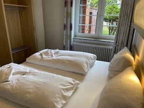 A double bed with white linens in a room with a window, a radiator, and a wooden wardrobe. - Holiday Apartment With 1 Bedroom (Wyk auf Foehr)