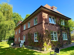 A two-story brick building with a flat roof, large windows, and a small garden area with a bench and outdoor furniture. - Holiday Apartment With 1 Bedroom (Wyk auf Foehr)