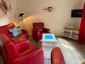 A living room with red leather sofas, a white coffee table, a floor lamp, a flat-screen TV, and a wall art piece. - Holiday Apartment With 1 Bedroom (Wyk auf Foehr)