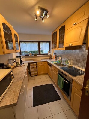 A kitchen with wooden cabinets, a black countertop, a window, and a tiled backsplash.