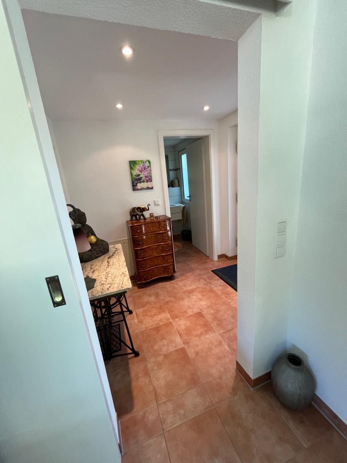 Un pasillo con un aparador de madera, una mesita y un jarrón decorativo.