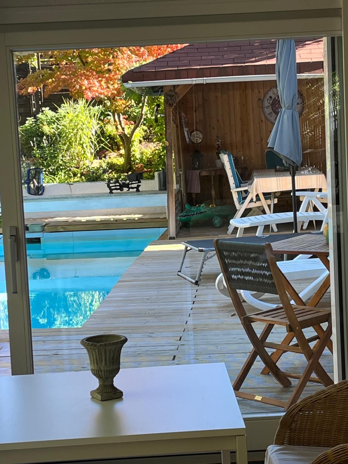 An outdoor pool area with a wooden deck, lounge chairs, and a table with a decorative bowl.