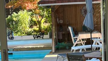 An outdoor pool area with a wooden deck, lounge chairs, and a table with a decorative bowl.