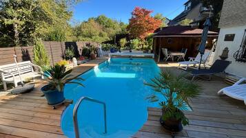 A swimming pool with a wooden deck, lounge chairs, and potted plants.