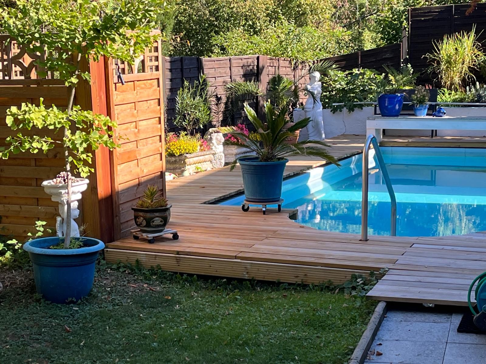 Ein Garten mit einer Holzterrasse, einem Schwimmbecken und verschiedenen Blumentöpfen.
