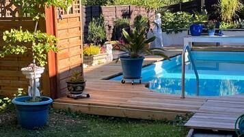 A backyard with a wooden deck, a swimming pool, and various potted plants.