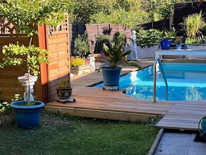 A backyard with a wooden deck, a swimming pool, and various potted plants.