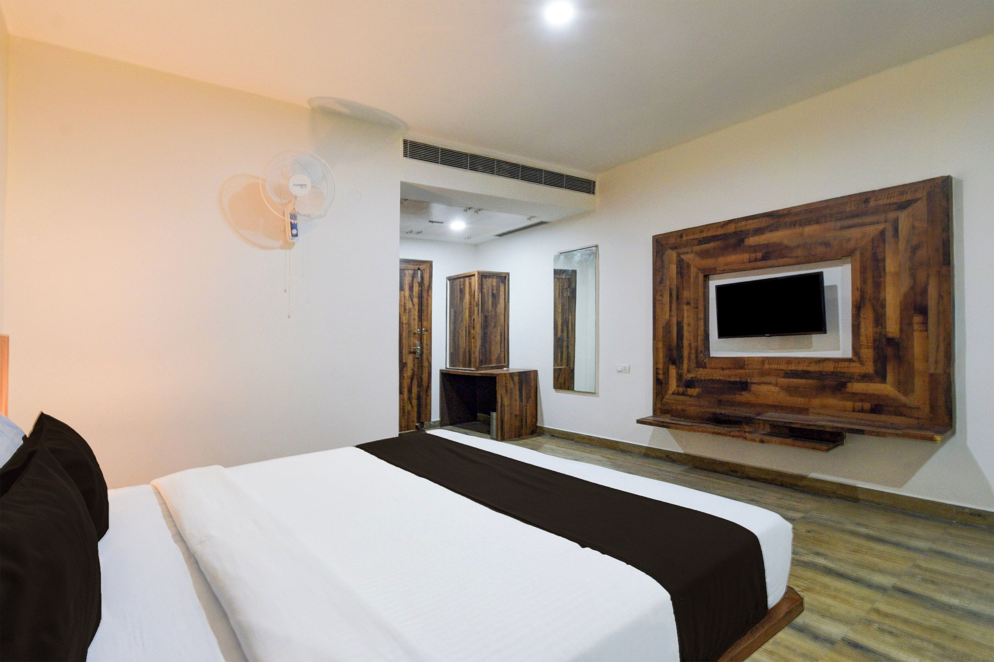 A hotel room with a bed, a TV mounted on the wall, and a wooden cabinet.