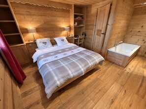 A wooden cabin bedroom with a bed, bedside lamps, a built-in shelf, a red curtain, and a wooden floor. - New Listing (Les Allues)