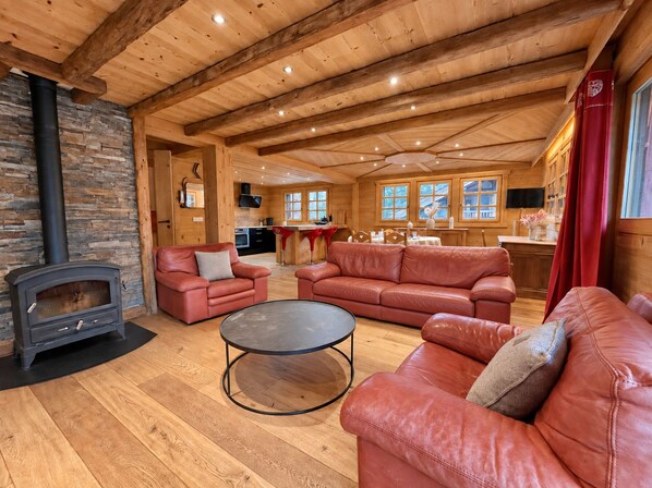 A cozy log cabin interior with a stone fireplace, leather sofas, a dining area, and a kitchen. - New Listing (Les Allues)