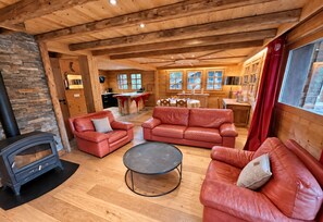 A cozy cabin interior with a stone wall, a fireplace, leather sofas, a dining area, and a kitchen. - New Listing (Les Allues)