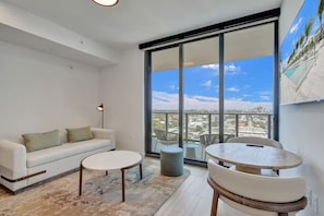 A modern living room with a sofa, two round tables, and a large window with a city view. - Miami Escape 1807 for 4 (Miami)