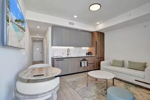 A modern living room with a white sofa, two round coffee tables, and a kitchen area with grey cabinets and a wooden accent wall. - Miami Escape 1807 for 4 (Miami)