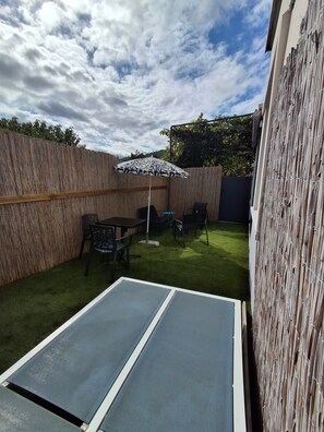Een achtertuin met een tafeltennistafel, twee stoelen, een klein rond tafeltje en een patroonrijke parasol.