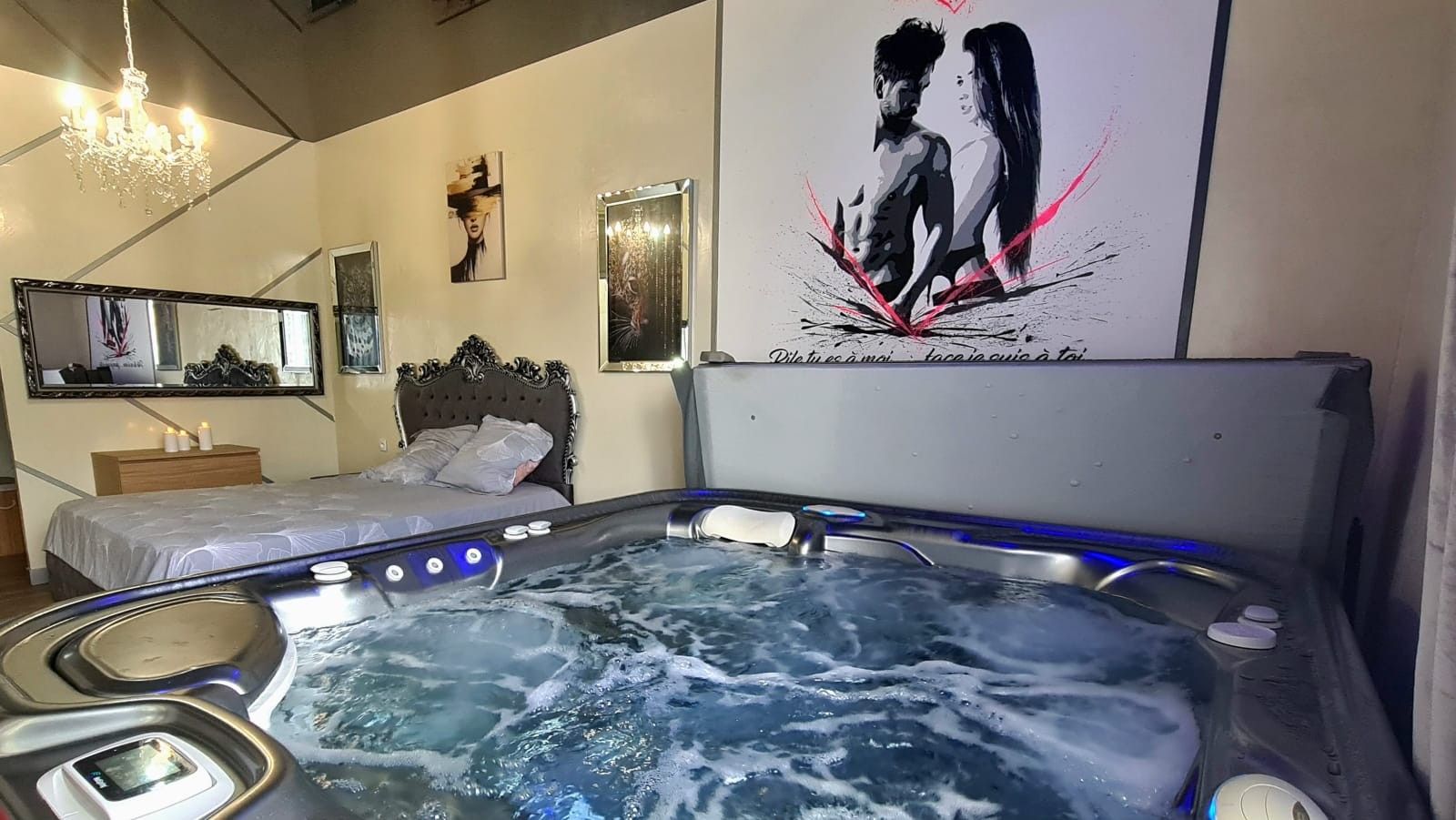 Een kamer met een ruime jacuzzi, een bed, een spiegel en wanddecoratie.