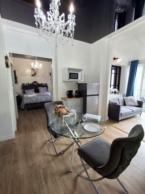 A modern interior with a dining area, a bed with a dark headboard, a living room with a grey sofa, and a chandelier. - Apartment 'La Discrète Romantique' with Hot Tub, Wi-Fi and Air Conditioning (Charavines)