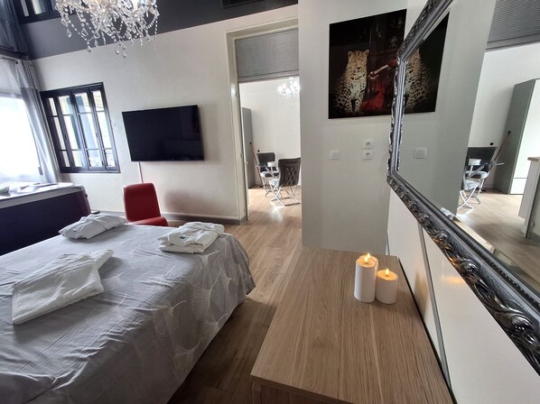 A hotel room with a bed, a TV, a mirror, and a chandelier. - Apartment 'La Discrète Romantique' with Hot Tub, Wi-Fi and Air Conditioning (Charavines)