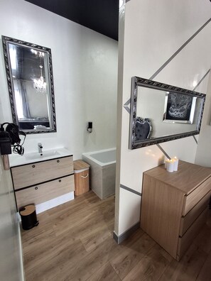 Een moderne badkamer met een wit wastafelmeubel, een badkuip en twee spiegels met decoratieve lijsten.