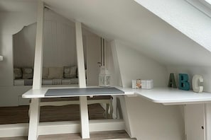 A white desk with a lamp, a shelf with letter blocks, and a built-in bench with cushions. - Captain's Dream Cabin (Harlesiel)