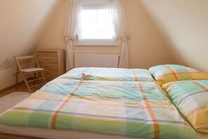 Ein Schlafzimmer mit Bett, Stuhl, Fenster und Heizkörper.