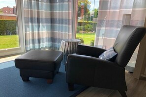 Ein Zimmer mit einem großen Fenster, einem schwarzen Ledersessel, einem passenden Hocker und einem kleinen runden Tisch.