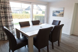 A dining area with a table and chairs, large windows, and a view of the outside. - Captain's Dream Cabin (Harlesiel)