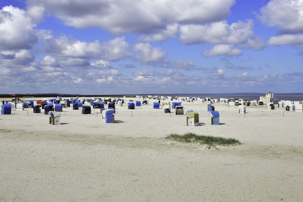 Ein Strand mit zahlreichen blauen und weißen Strukturen, vermutlich Briefkästen oder Kiosken, und einem klaren Himmel mit Wolken.