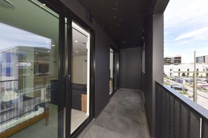 A narrow corridor with glass doors leading to a room, a tiled floor, and a view of a parking area with buildings in the background. - Christchurch City Studio With Private Balcony (Christchurch)