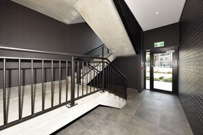 A modern staircase with metal railings, a black brick wall, and a glass door leading outside. - Christchurch City Studio With Private Balcony (Christchurch)